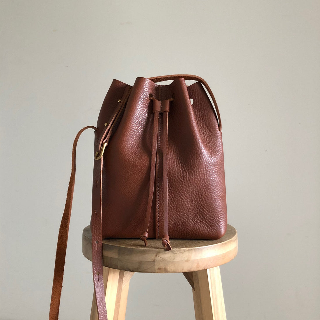 A tan coloured leather bag sitting on a wooden stool