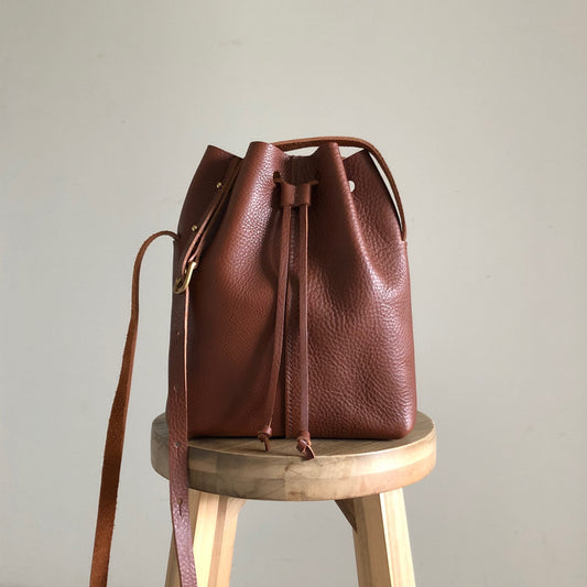 A tan coloured leather bag sitting on a wooden stool