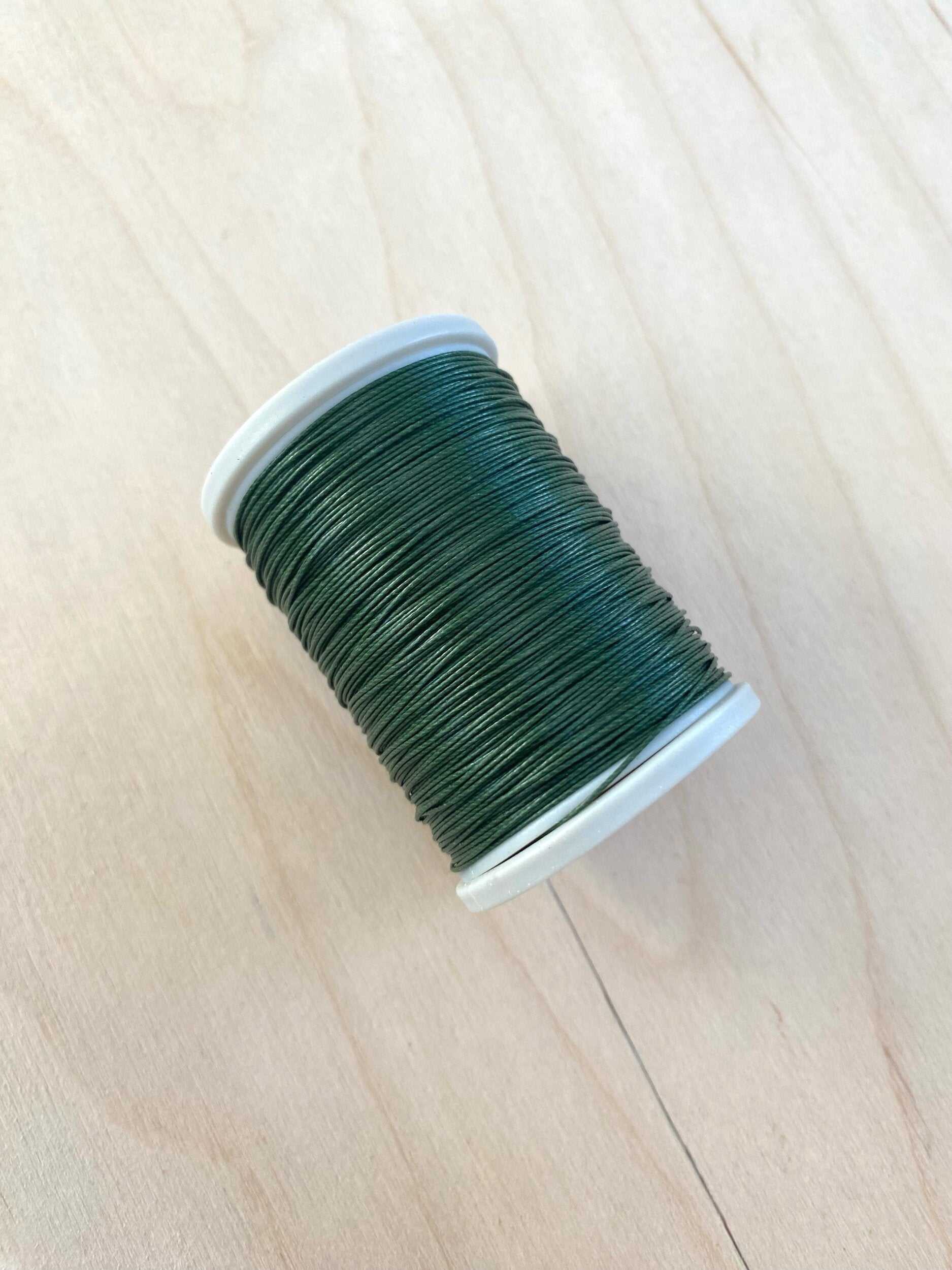 Green cotton linen thread spool 0.55 mm on light wood background.