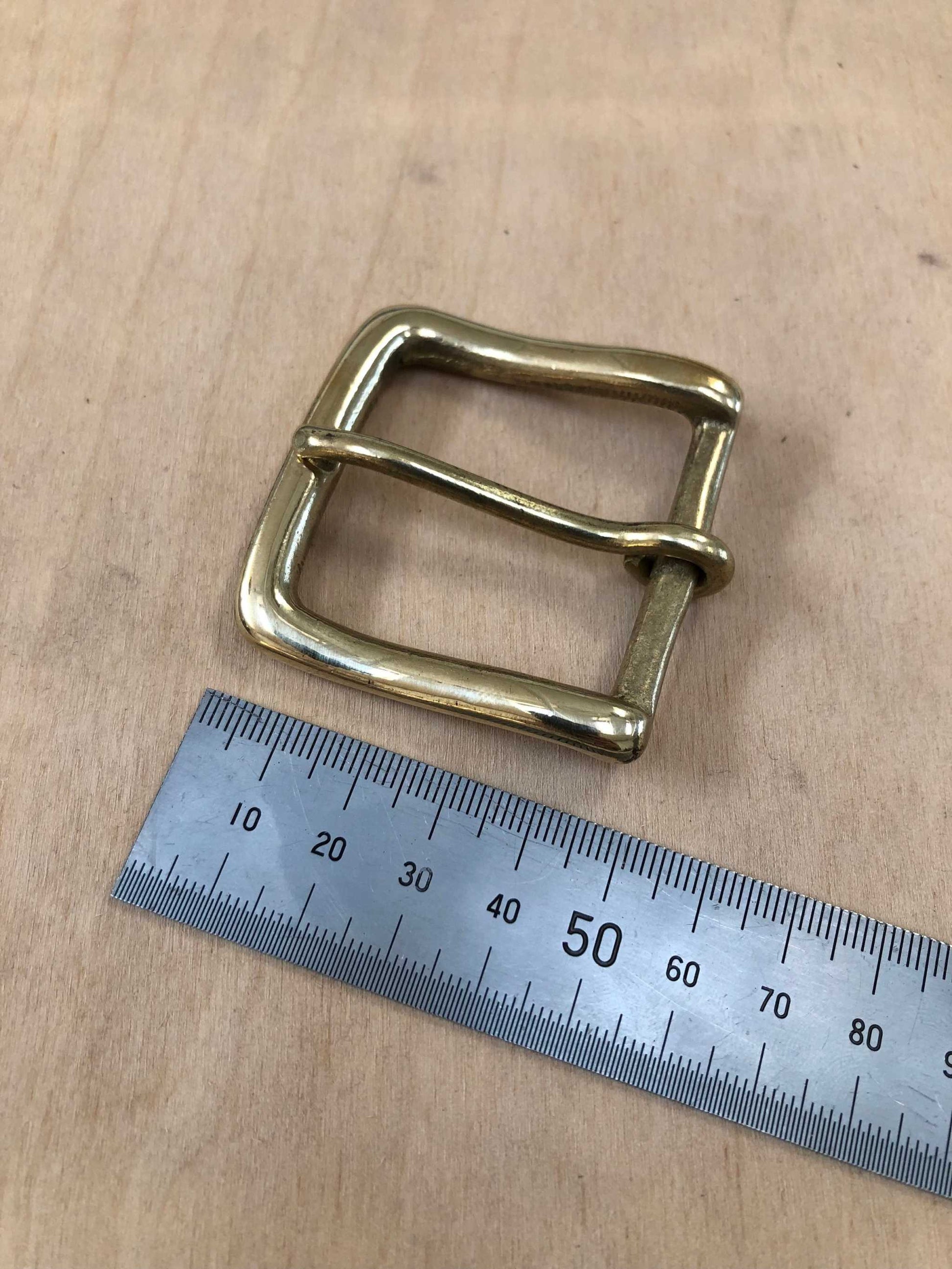 Solid brass belt buckle with rounded frame and pin, shown with a ruler for size reference.