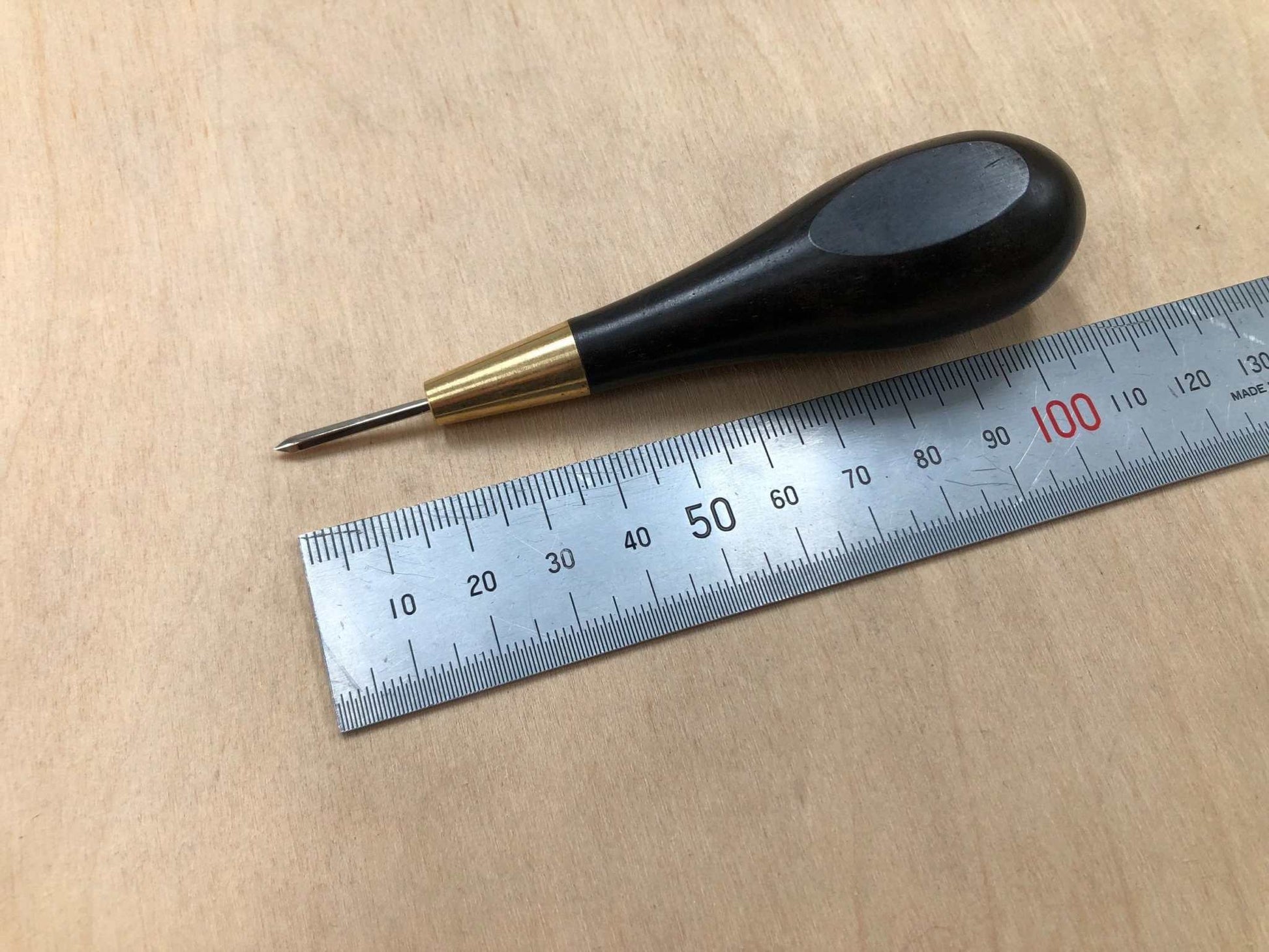 Wooden handled stitching awl with black ebony finish and ergonomic design next to a ruler.