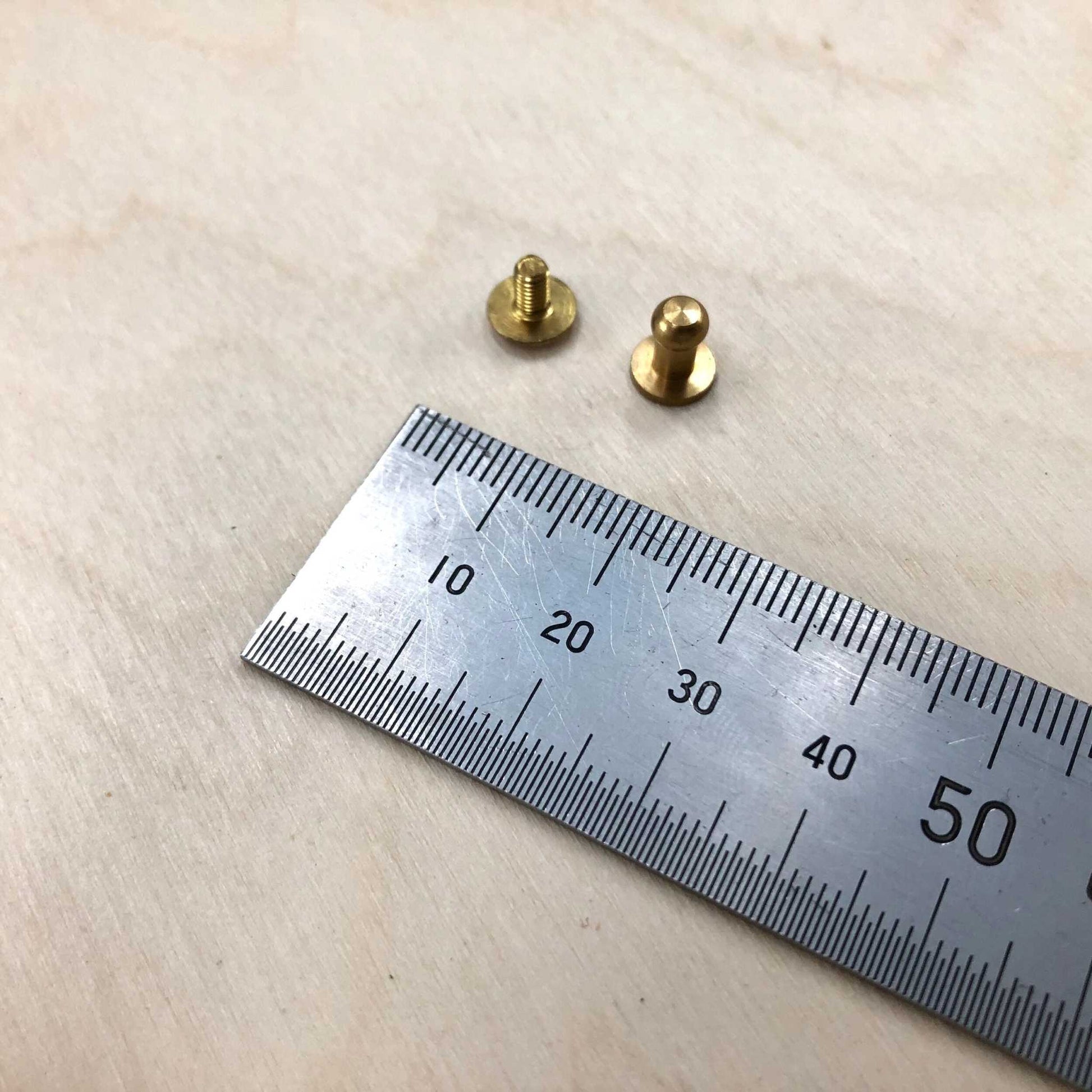 Solid brass Sam Browne studs with screws next to a ruler for size reference.