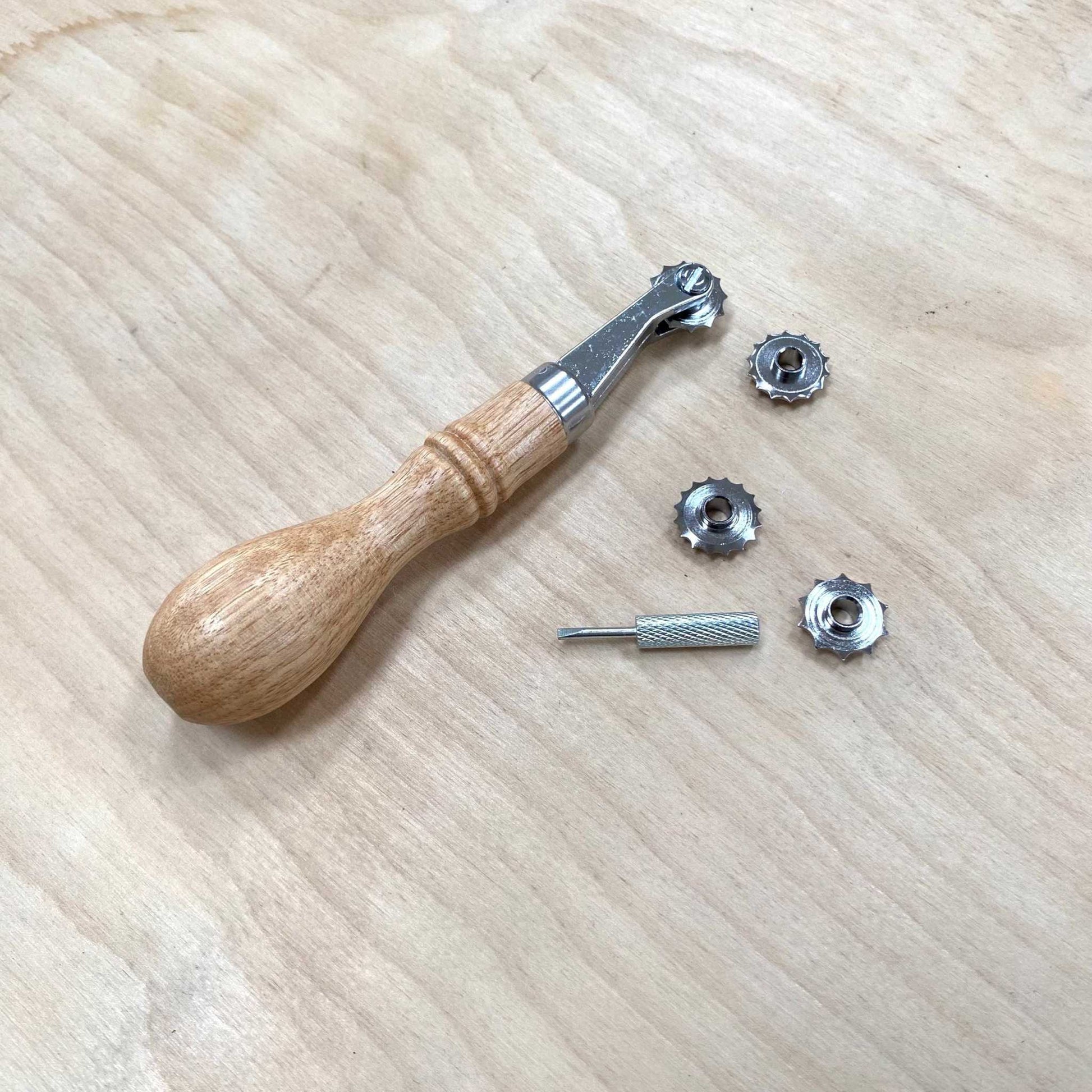 Leather Hand Stitch Spacer 4-in-1 tool with wooden handle and interchangeable metal heads on a wooden surface.