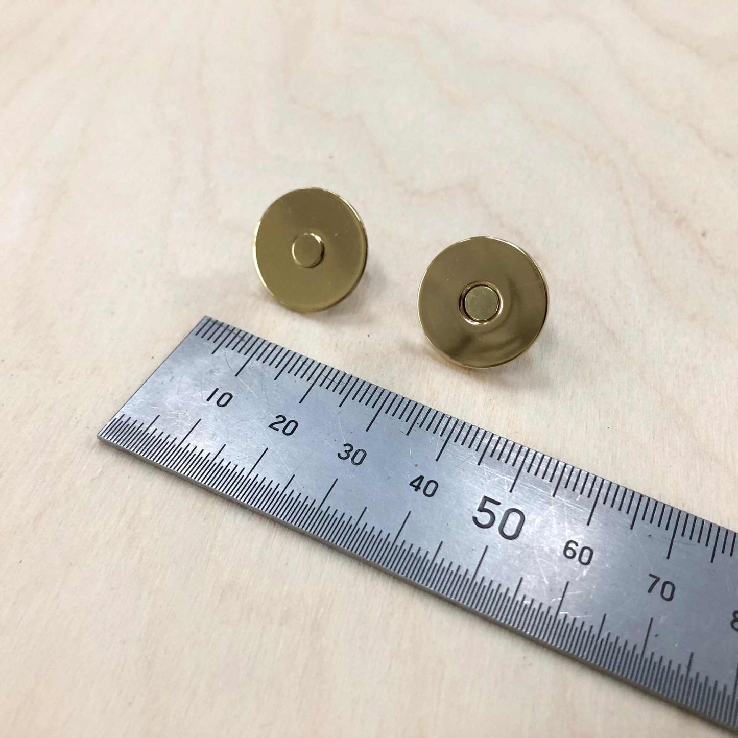 Gold magnetic snap fasteners next to a ruler, size 13mm diameter.