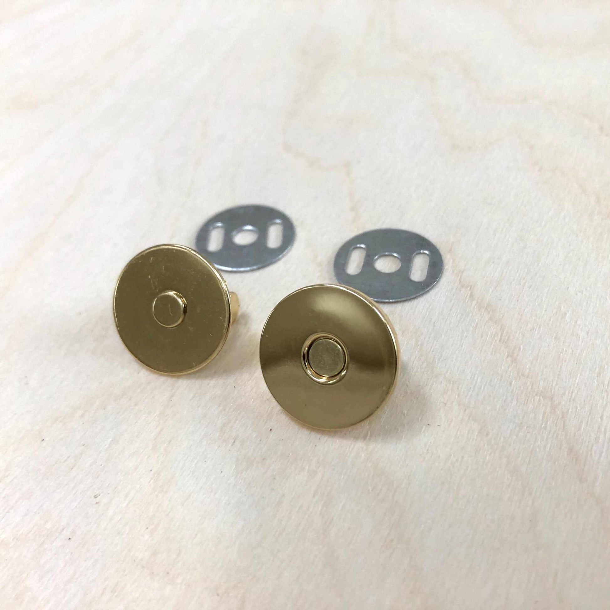 Magnetic snap fasteners in gold with back plates on light wood surface.