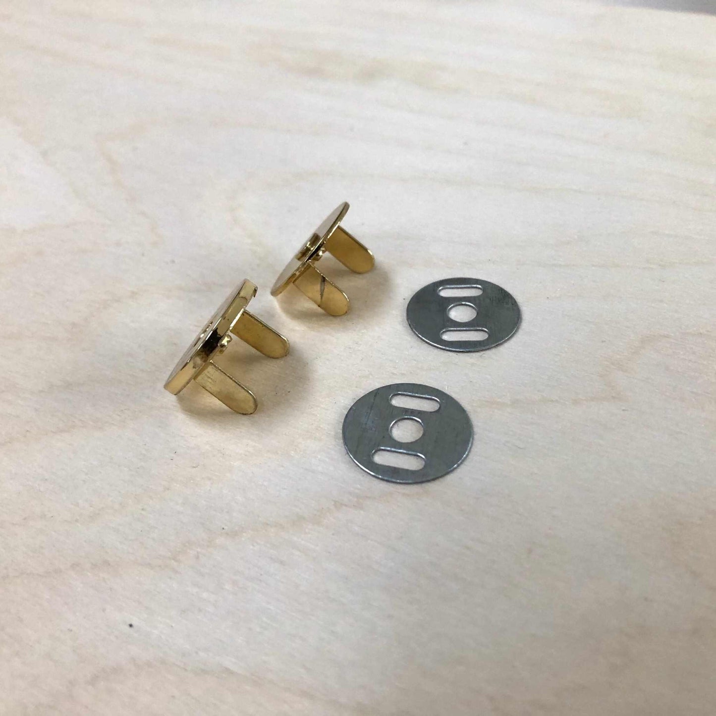 Gold and silver magnetic snap fasteners with back plates on a wooden surface.