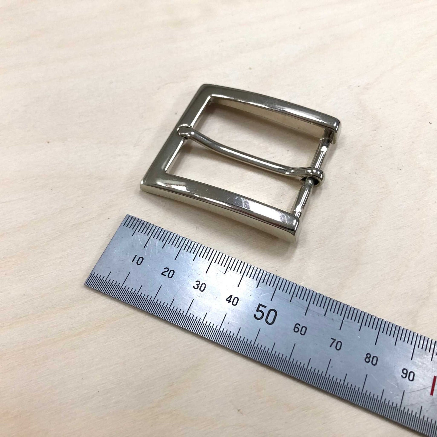 Square silver chrome belt buckle with polished finish and pin, 34mm internal width by 51mm length, beside a ruler.