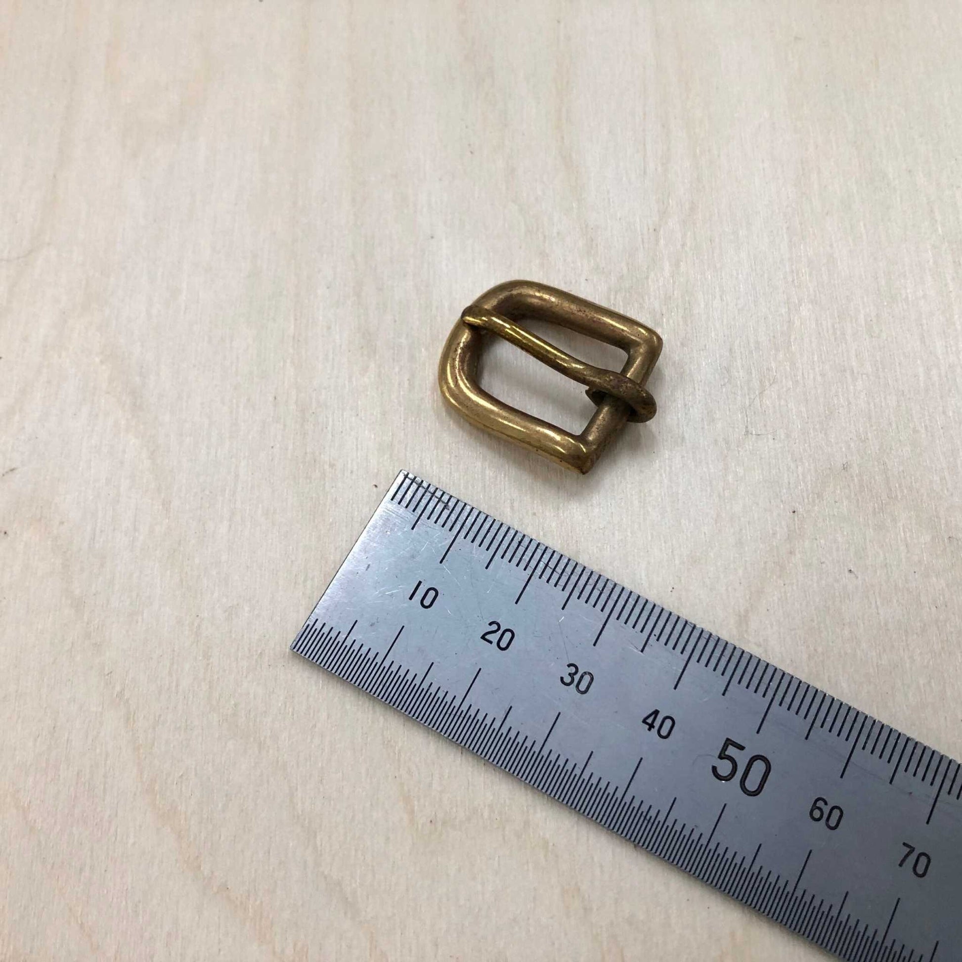 Solid Brass Belt Buckle next to a ruler for size reference, showcasing its rounded frame and pin style.