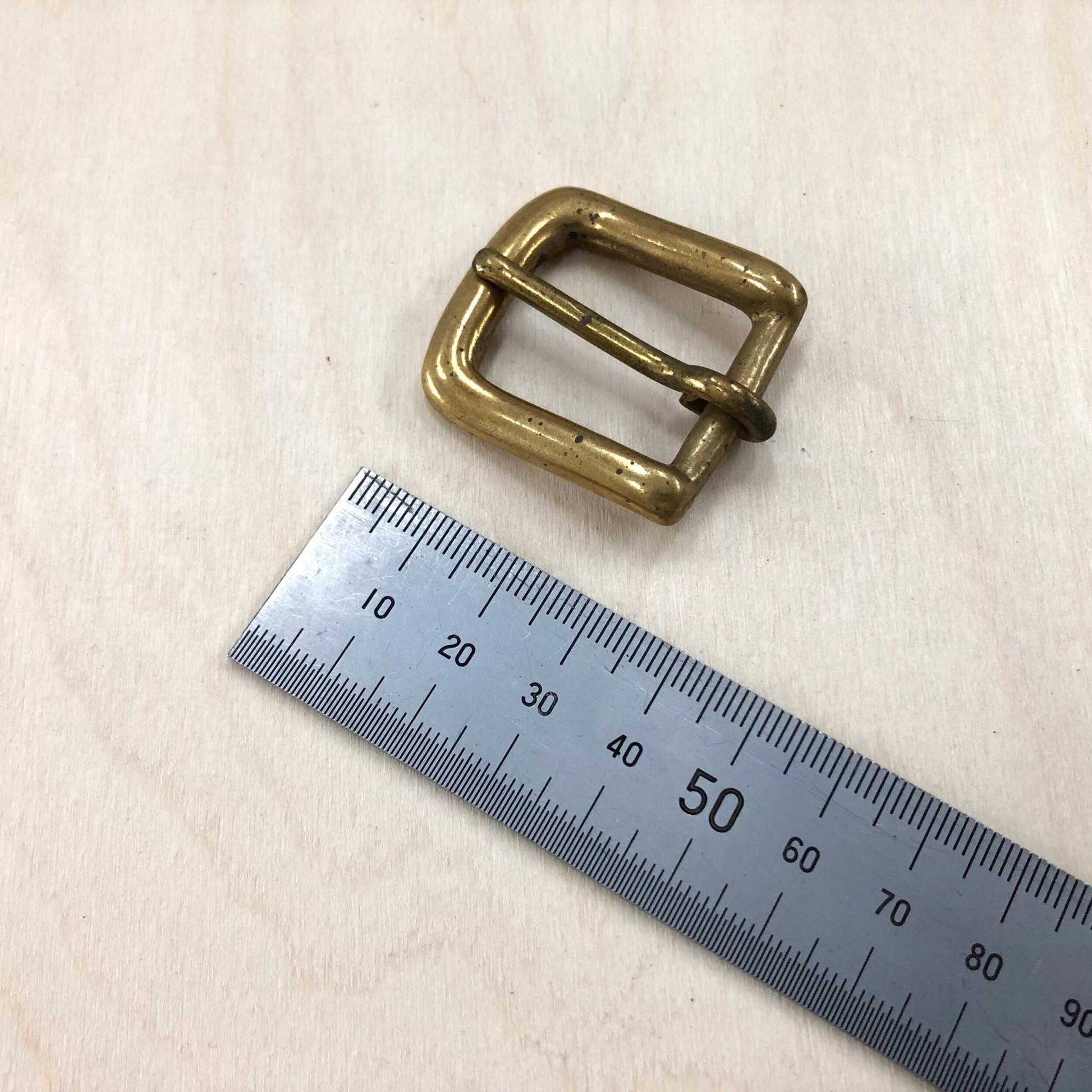 Solid brass belt buckle with rounded frame, featuring a pin style; ruler indicates various sizes.