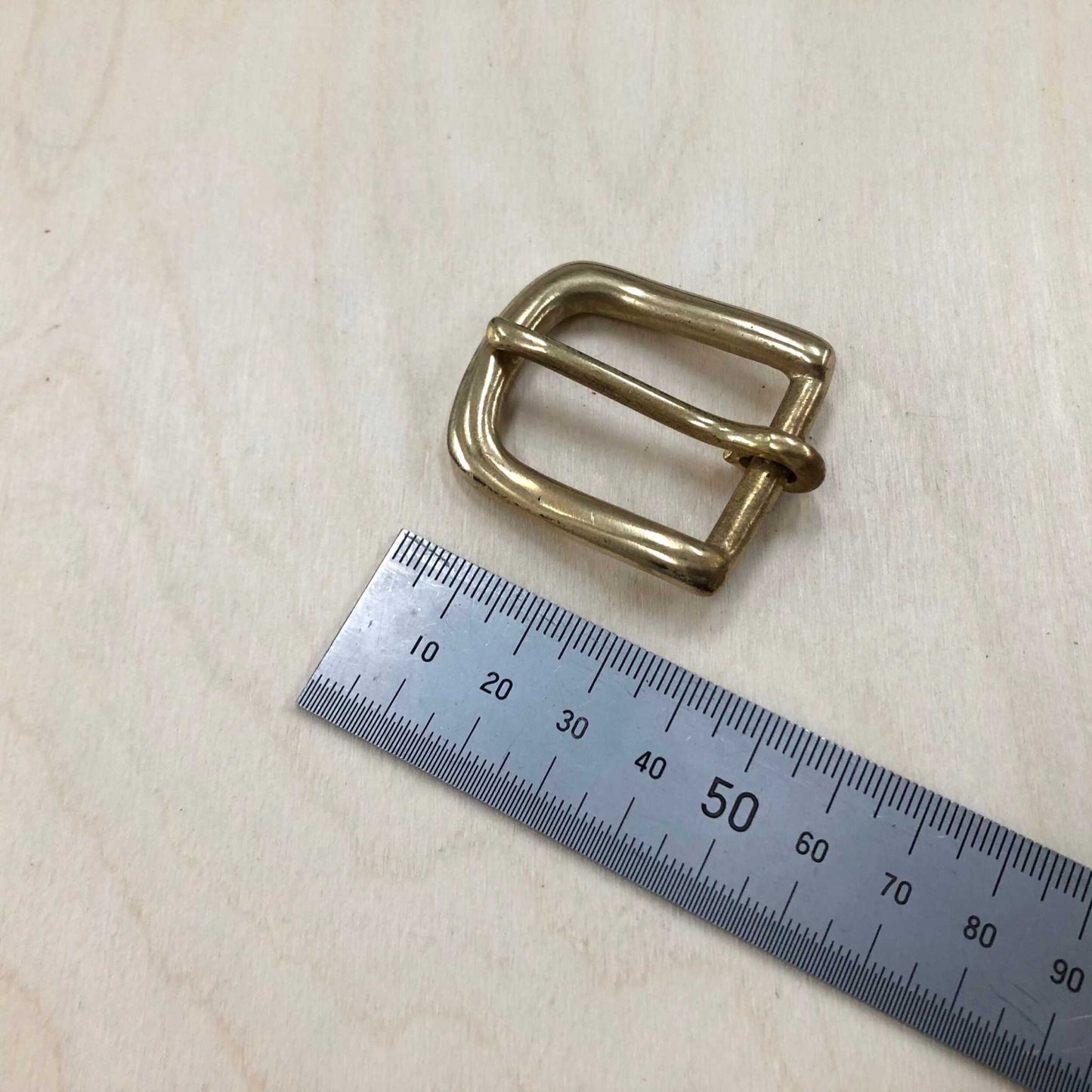 Solid Brass Belt Buckle with rounded frame and pin on wooden surface with ruler for size reference.