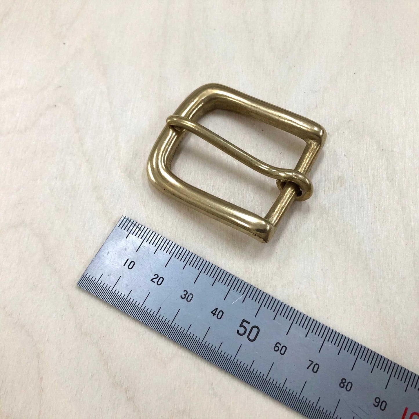 Solid brass belt buckle with rounded frame and pin, next to ruler for size reference.