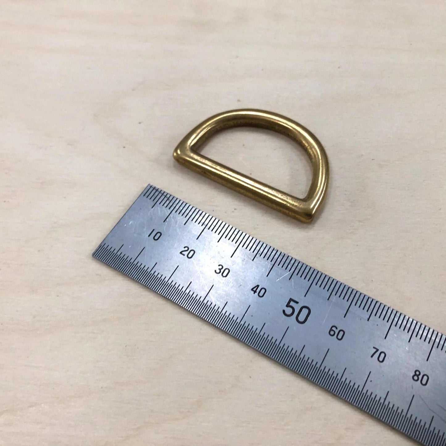 Solid brass D ring with a measuring ruler for size reference.