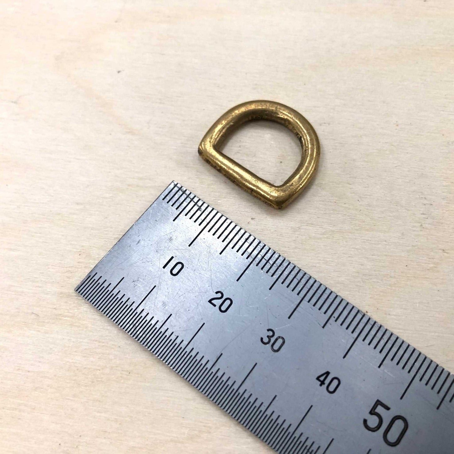 Solid brass D ring with ruler for size reference, ideal for leather crafting.